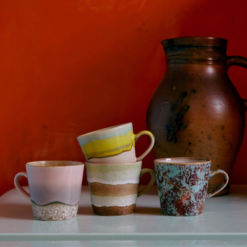 Set of ceramic mugs and a pitcher on a white surface with an orange wall background