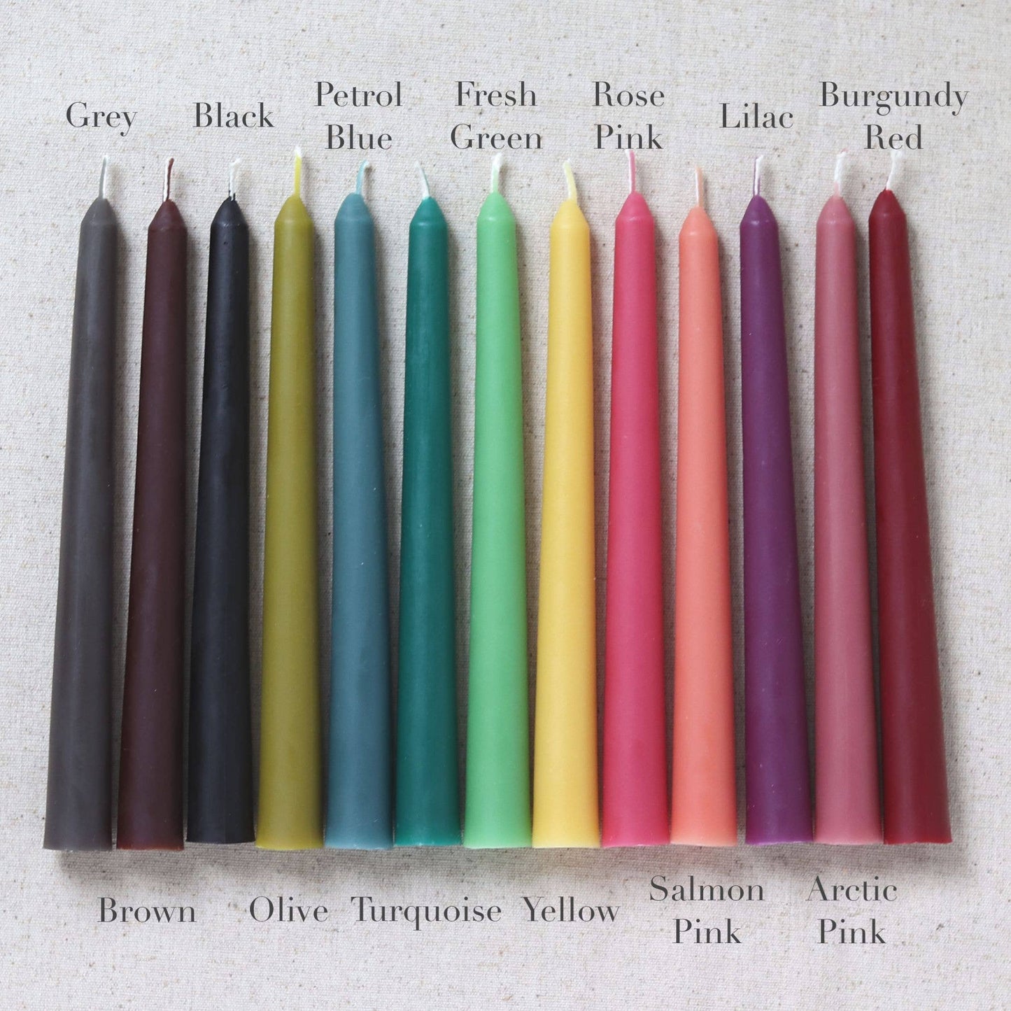Row of colorful beeswax candles in various colors with labels on a textured background