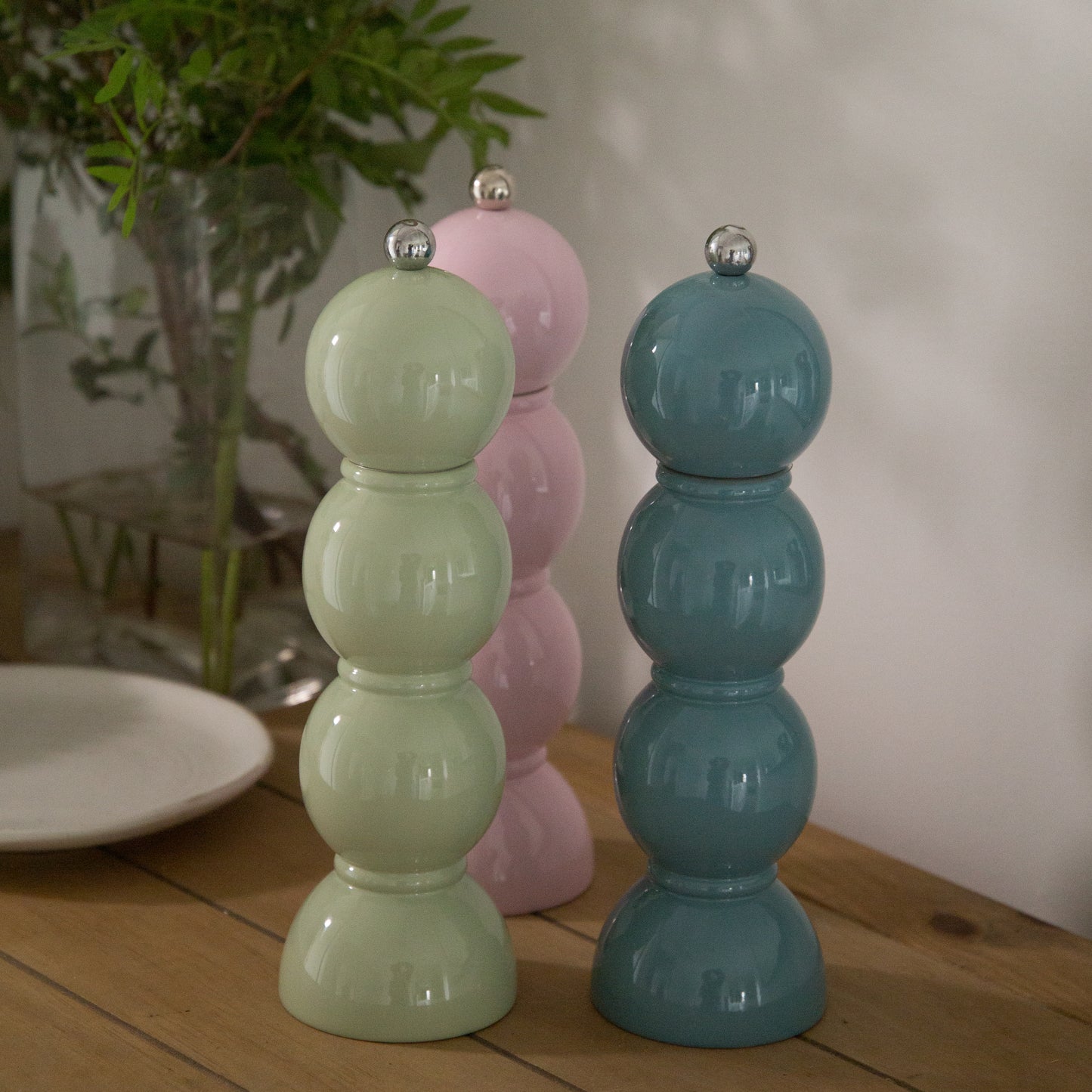 Three colorful salt and pepper shakers on a wooden surface with a blurred indoor background.