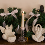 Decorative setup with a lit candle, angel figurines, and Christmas wreath.