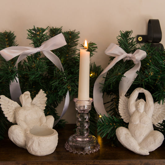 Decorative setup with a lit candle, angel figurines, and Christmas wreath.