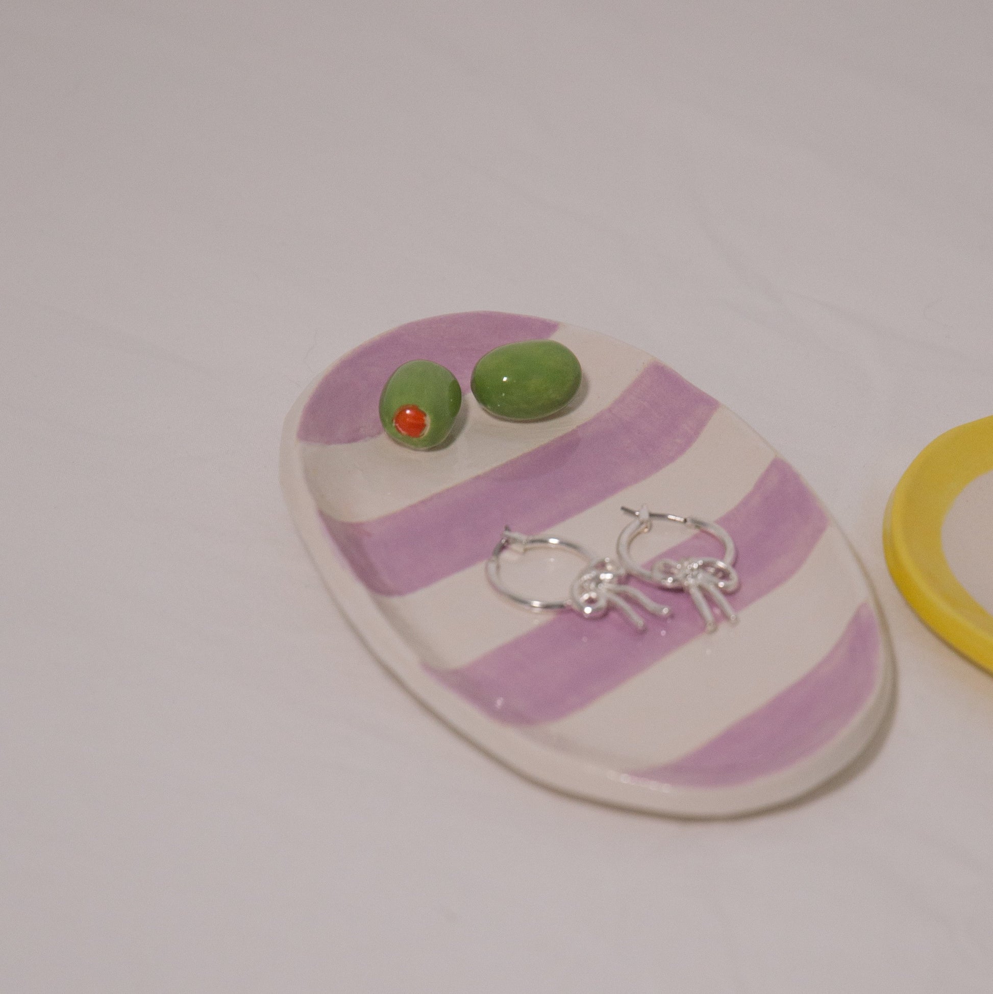 Striped pink and white ceramic dish with green and red earrings on a white background