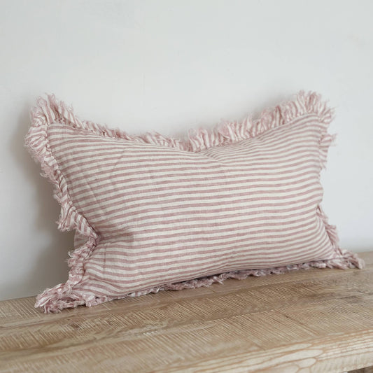Striped pillow with ruffled edges on a wooden surface against a white wall