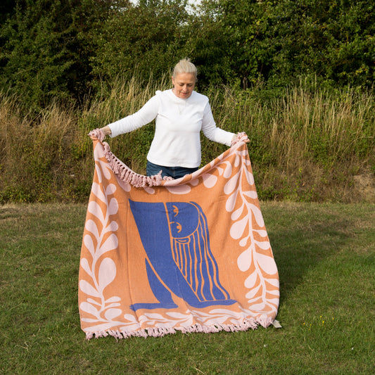 Person holding a large decorative blanket with a logo in an outdoor setting