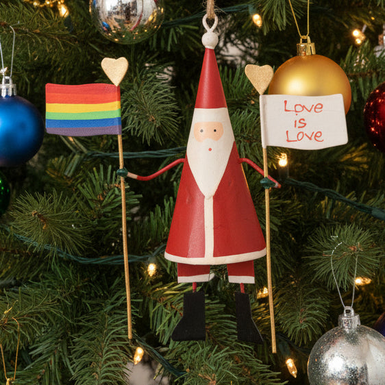 Decorative figure of Santa Claus holding a rainbow flag and 'Love is Love' sign on a beige background