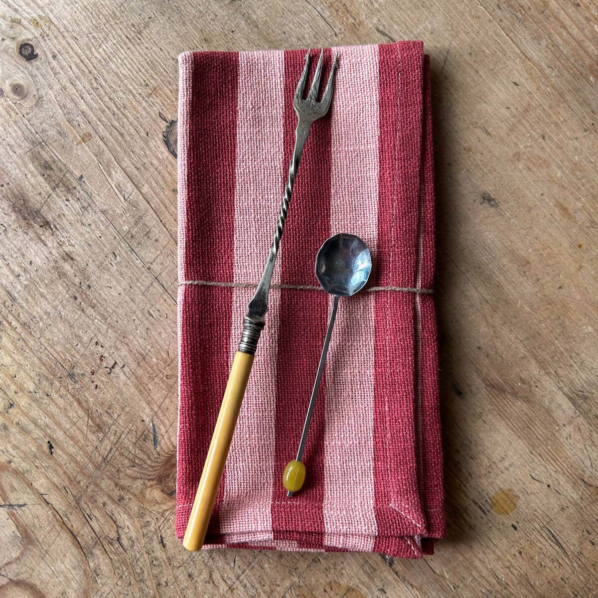 Folded red and white striped towel with a fork and spoon on a wooden surface