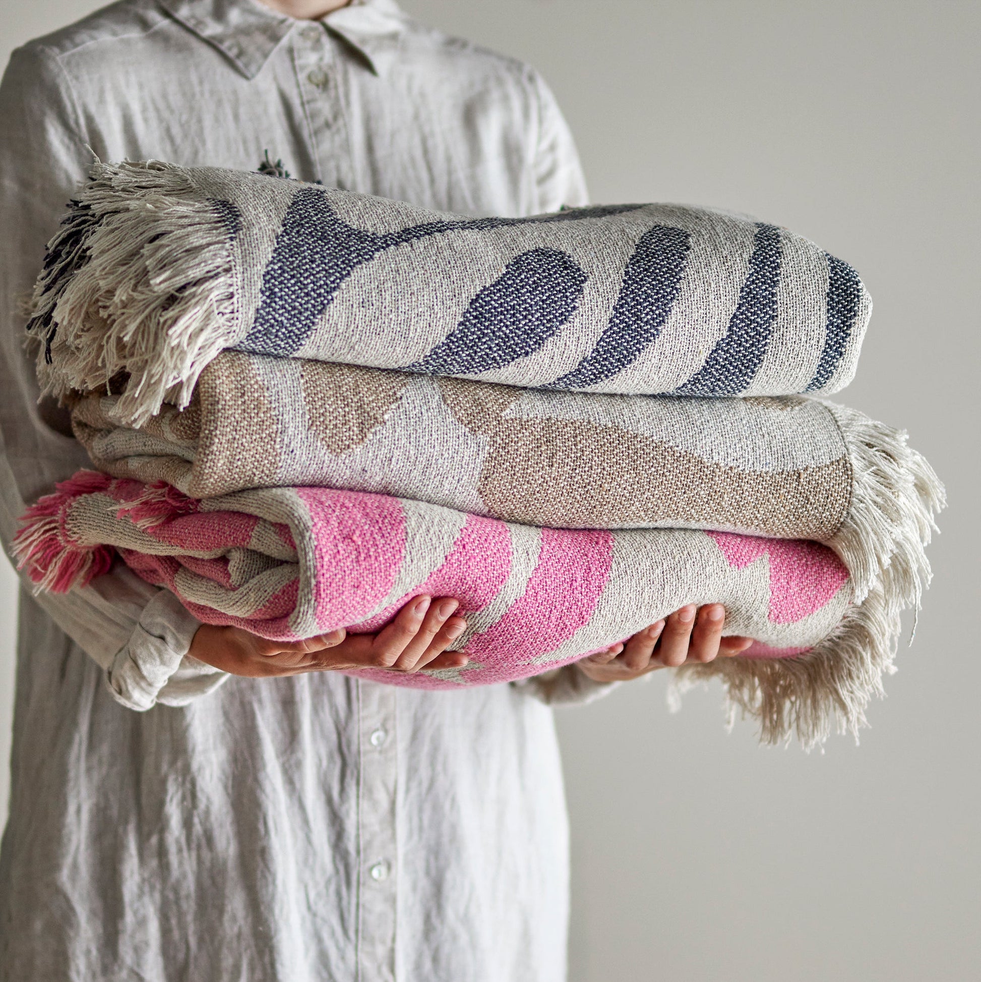 Bloomingville recycled cotton throw displayed with other throws in similar colours by a female model holding them 