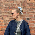 Woman wearing a blue denim jacket and green top with a silver chain bag against a brick wall.