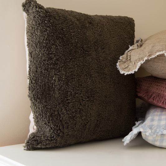 Stack of various textured pillows on a white surface with a neutral background