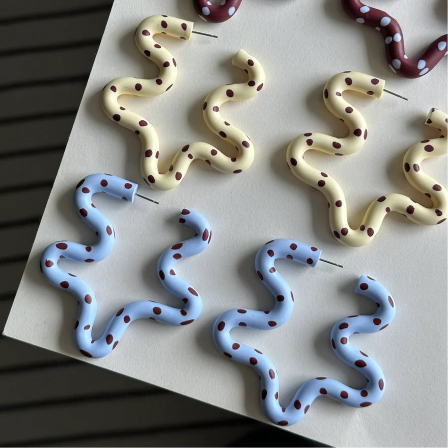 Snake-shaped earrings in various colors on a white surface.