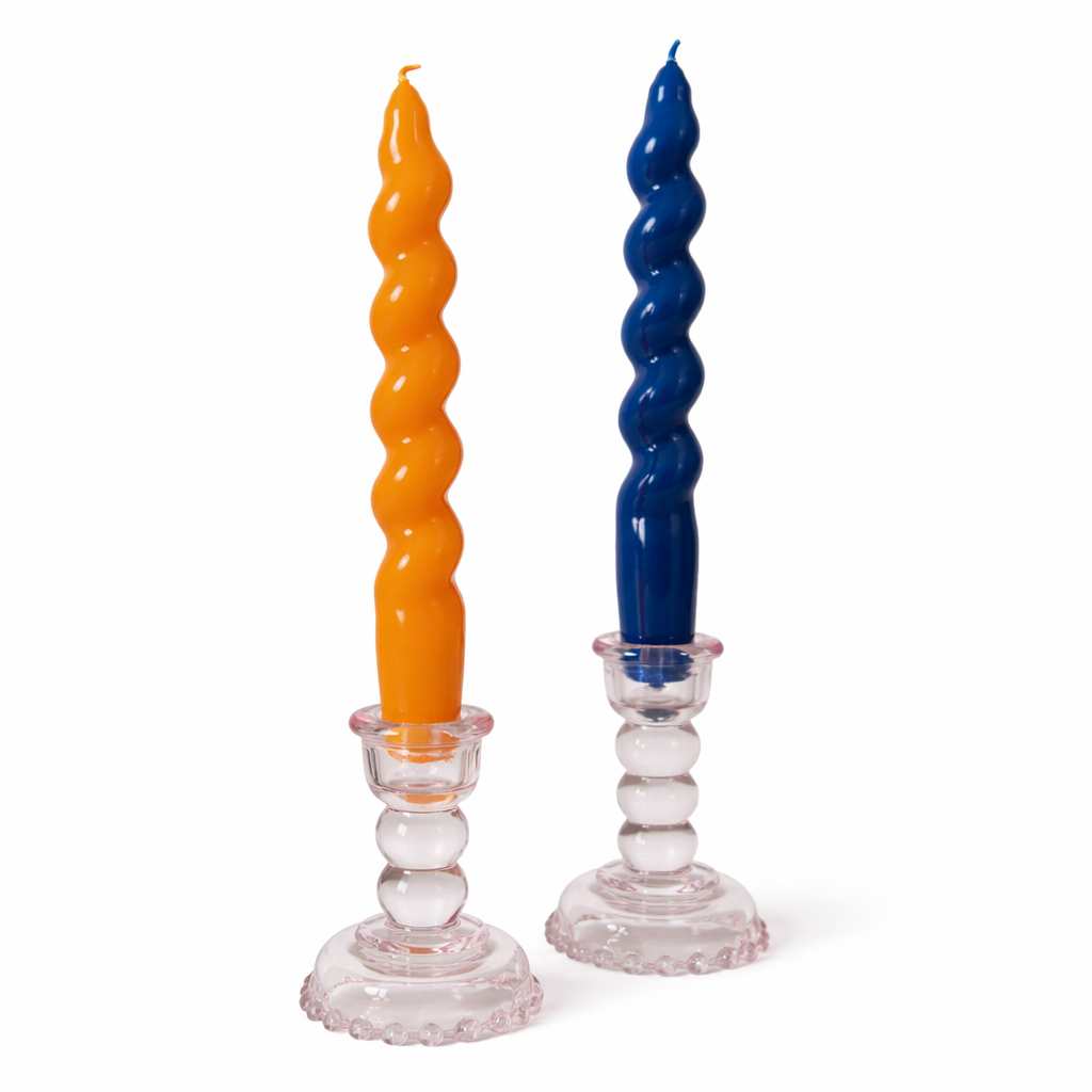 Two twisted candles, one orange and one blue, on clear candlesticks against a white background.