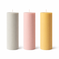 Three ribbed pillar candles in beige, pink, and orange colors, made from soy wax, displayed on a white surface against a neutral background.
