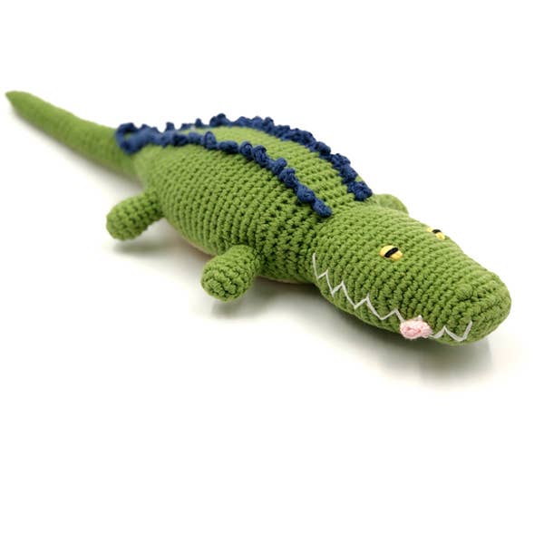 Handmade crochet crocodile baby rattle laying on a white background. 