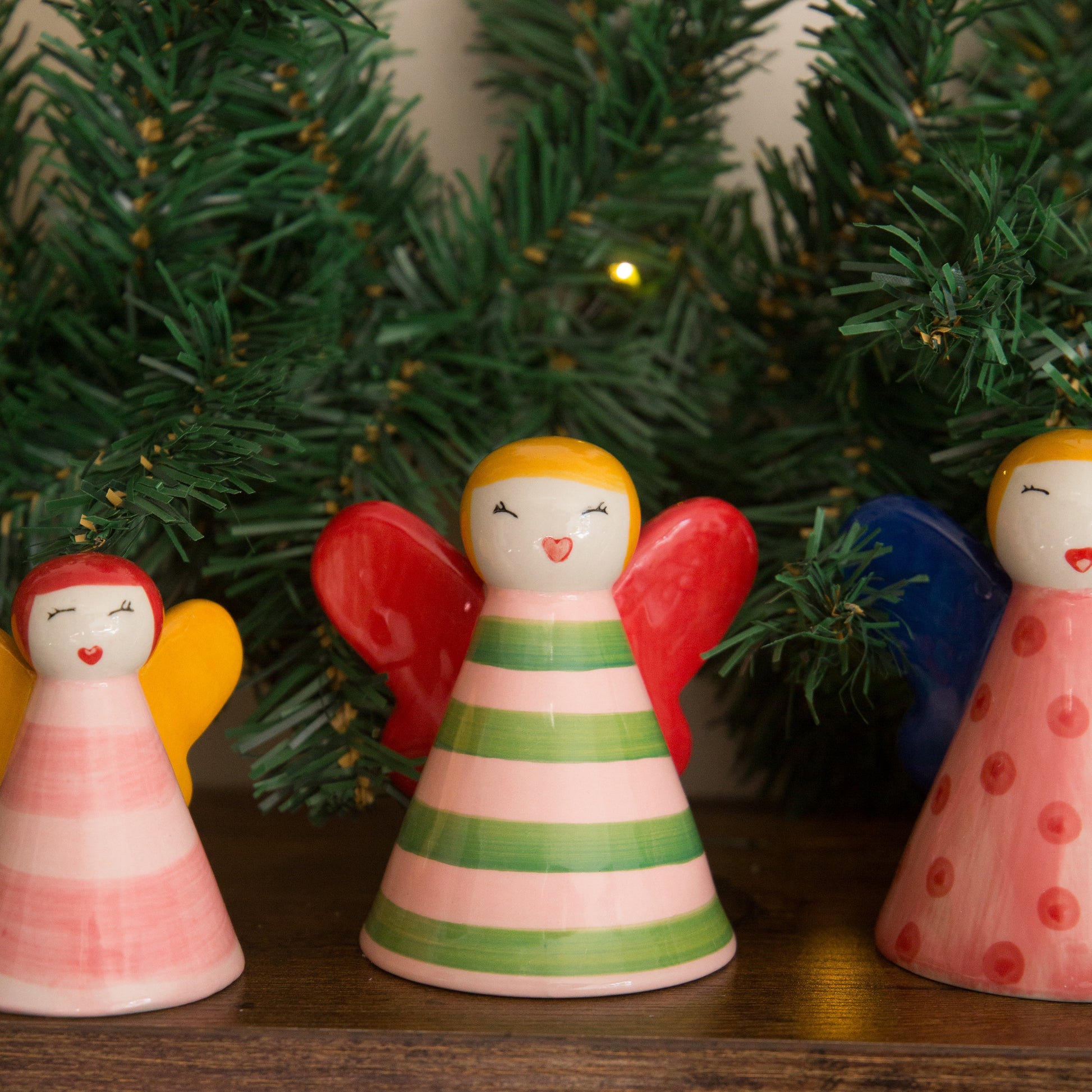 Decorative angel figurines with colorful wings in front of a Christmas tree.