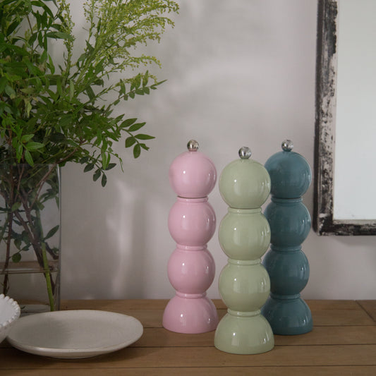 Three colorful ceramic vases on a wooden surface with a plant in the background.