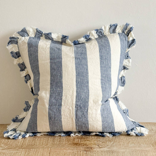 Ellenvale Hallie Ruffled Edged Linen Cushion in Blue Wide Stripe displayed on a bench against a white wall.
