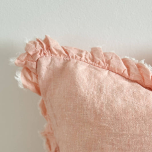 Ellenvale Ruffled Edge Linen Cushion in Washed Pink displaying the corner detail of the cushion against a white wall.