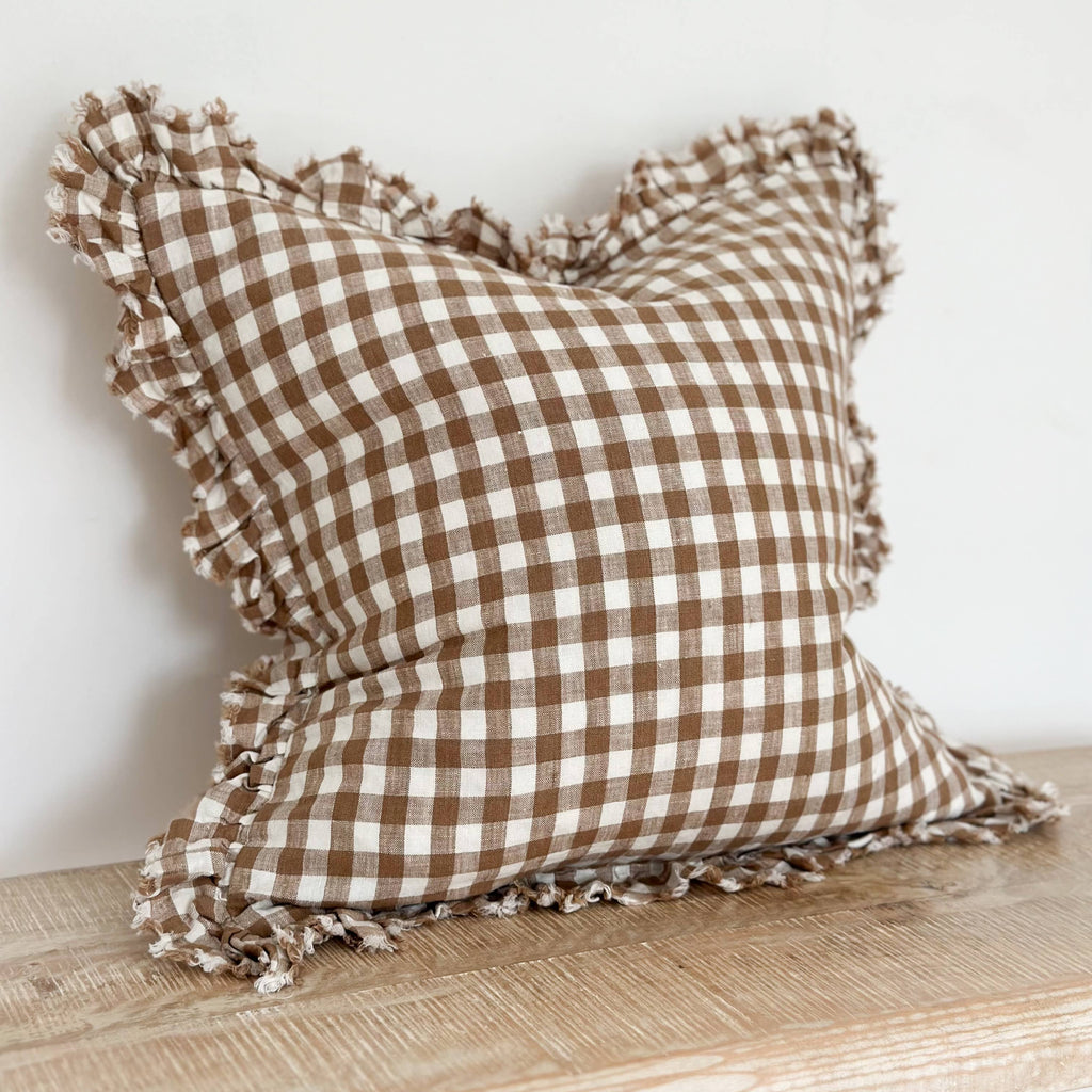 Ellenvale Ruffled Edged Linen Cushion Cover in Brown Gingham displayed on a bench against a white wall.