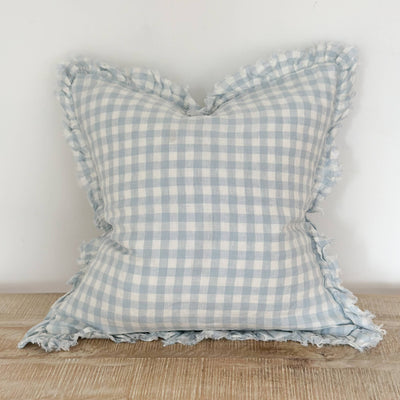 Light blue linen gingham cushion with ruffled edge by Ellenvale displayed on a bench against a white wall