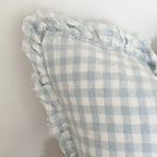 Ellenvale Ruffled Linen Cushion in Blue Gingham with a ruffle edge displayed on a bench against a white wall.