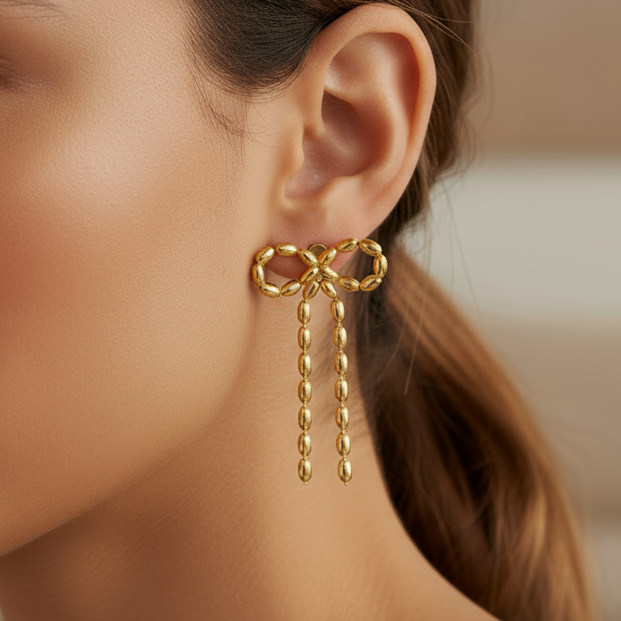 Close-up of a woman wearing gold bow-shaped earrings with dangling beads.