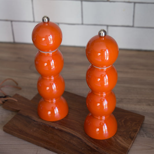 Two orange salt and pepper shakers on a wooden surface with a tiled wall background.