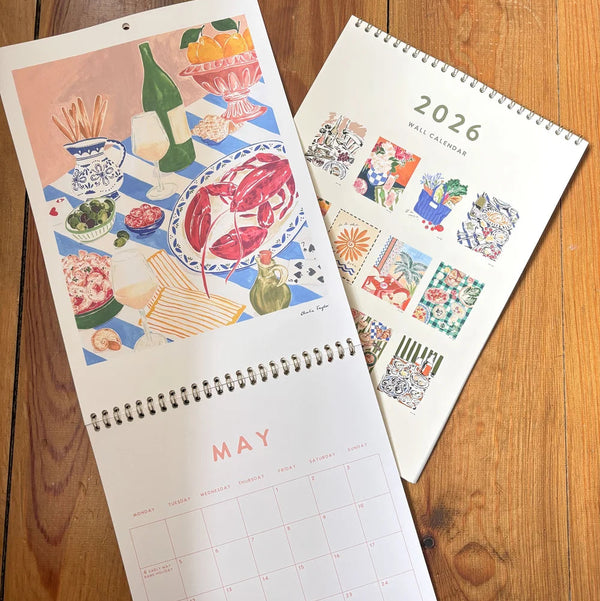 Two calendars on a wooden surface, one open to May and the other showing a grid for 2026.