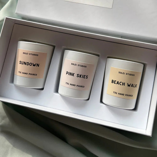 Three candles in a box with 'Solei Studios' branding on a soft fabric background.
