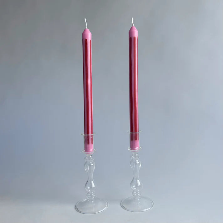 Two pink candles in glass candlesticks on a gray background
