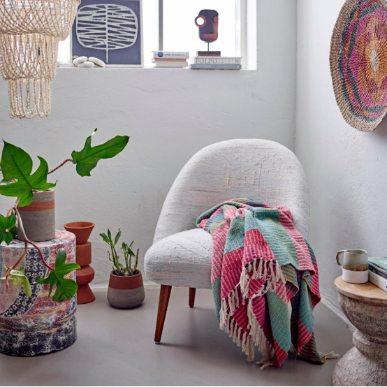 Cozy living room with a white armchair, colorful blanket, and decorative items.