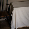 White textured throw blanket on a wooden chair against a plain wall.