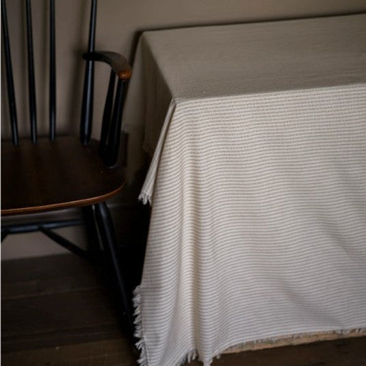 White textured throw blanket on a wooden chair against a plain wall.