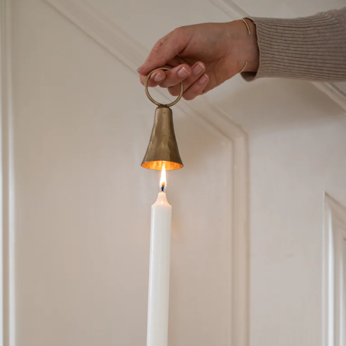 Brass Bell shaped candle snuffer, held over the top of a white lit taper candle ready to extinguish.