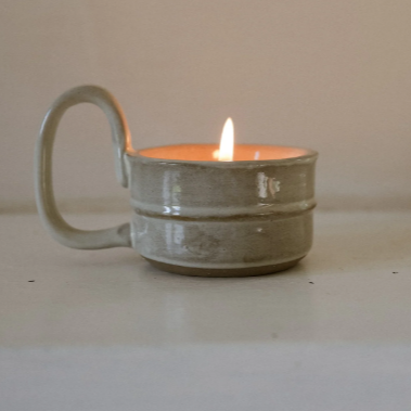Candle Cup Holder in milky white with handle displayed with a tea light burning. Vinage and artisan feel. 