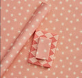 Pink wrapping paper with white star pattern and folded pink wrapping paper with geometric pattern on a matching background.