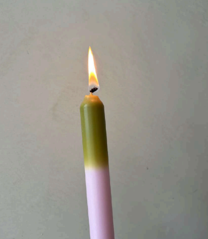 Pygmalion Dinner Candle Pink with green ombre candle in photo shown as lit with a bright orange flame 