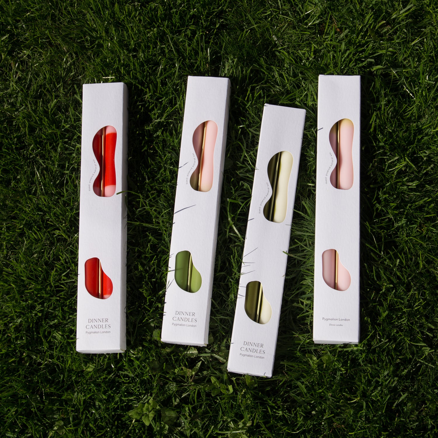set of two dinner candles displayed in their boxes lay next to each other on the grass. Showing the front packaging and the styles in stock. 
