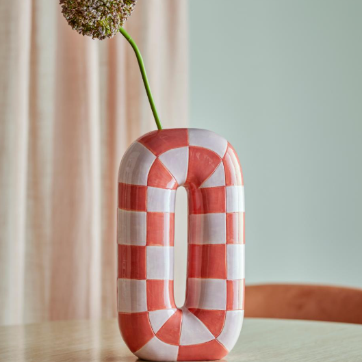 Red and white checkered vase with a single flower on a light surface.
