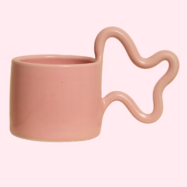 Pink ceramic mug with a unique handle design on a light pink background