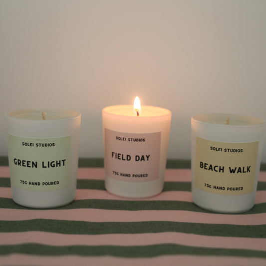 Solei Studios Mini Jar Candles in summer scents displayed with one burning and the others next to it. They are all displayed on a green and pink table cloth 