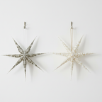 Two white paper Christmas decorations shaped like stars with painted patterns, ready to hang.