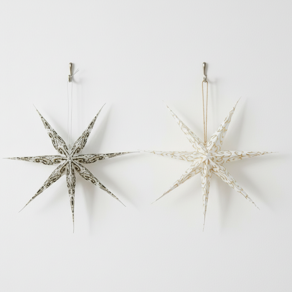 Two white paper Christmas decorations shaped like stars with painted patterns, ready to hang.