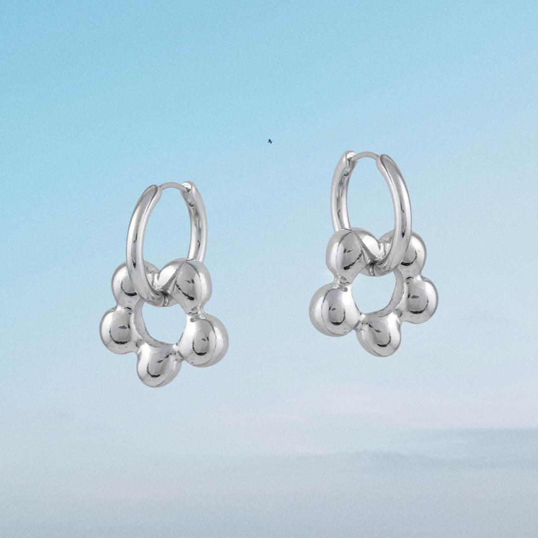 Silver hoop earrings with spherical ends against a light blue background