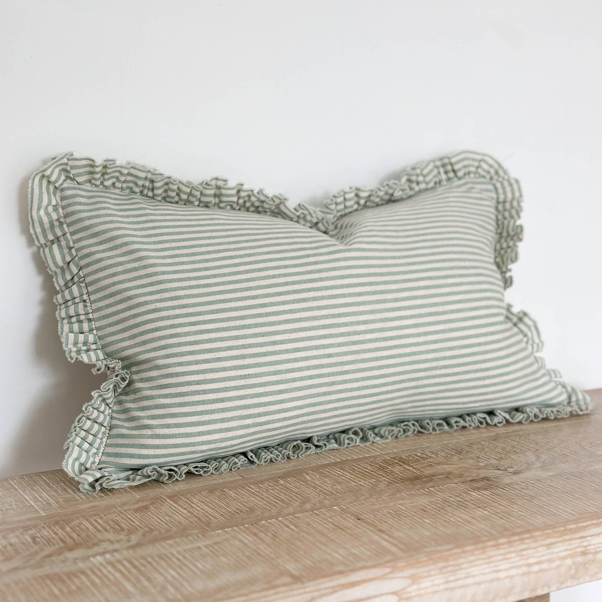 Striped pillow with ruffled edges on a wooden bench against a white wall