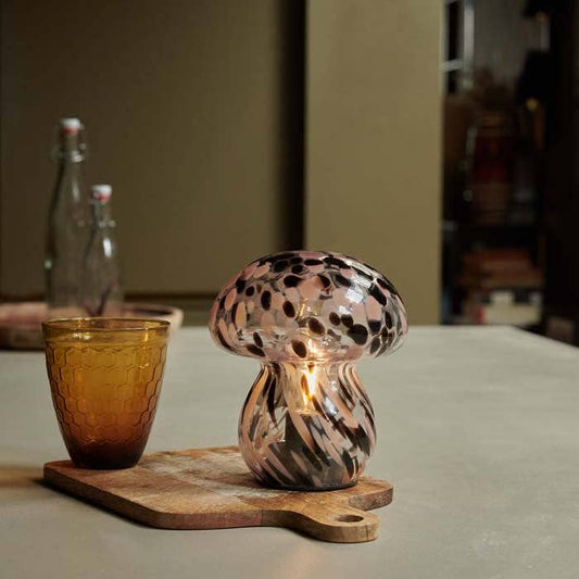 Mushroom-shaped glass lamp on a wooden board with an amber glass cup in a dimly lit room.