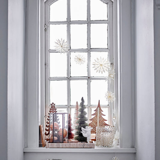 Decorative window sill with Christmas trees and ornaments against a light gray wall.