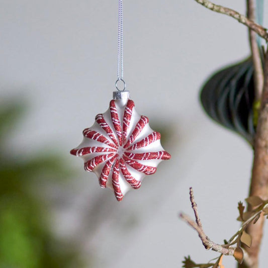 A red and white striped Christmas ornament hanging on a tree, with a blurred background of foliage.