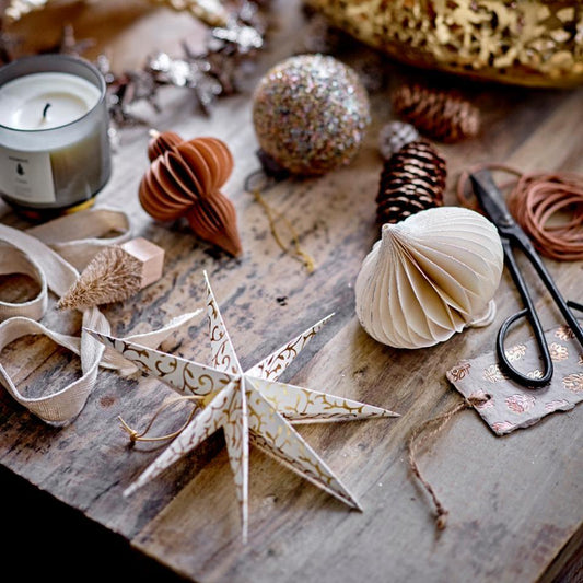 A collection of paper Christmas decorations displayed on a wooden surface, including a star with gold accents, pine cone shapes, and other holiday-themed items.