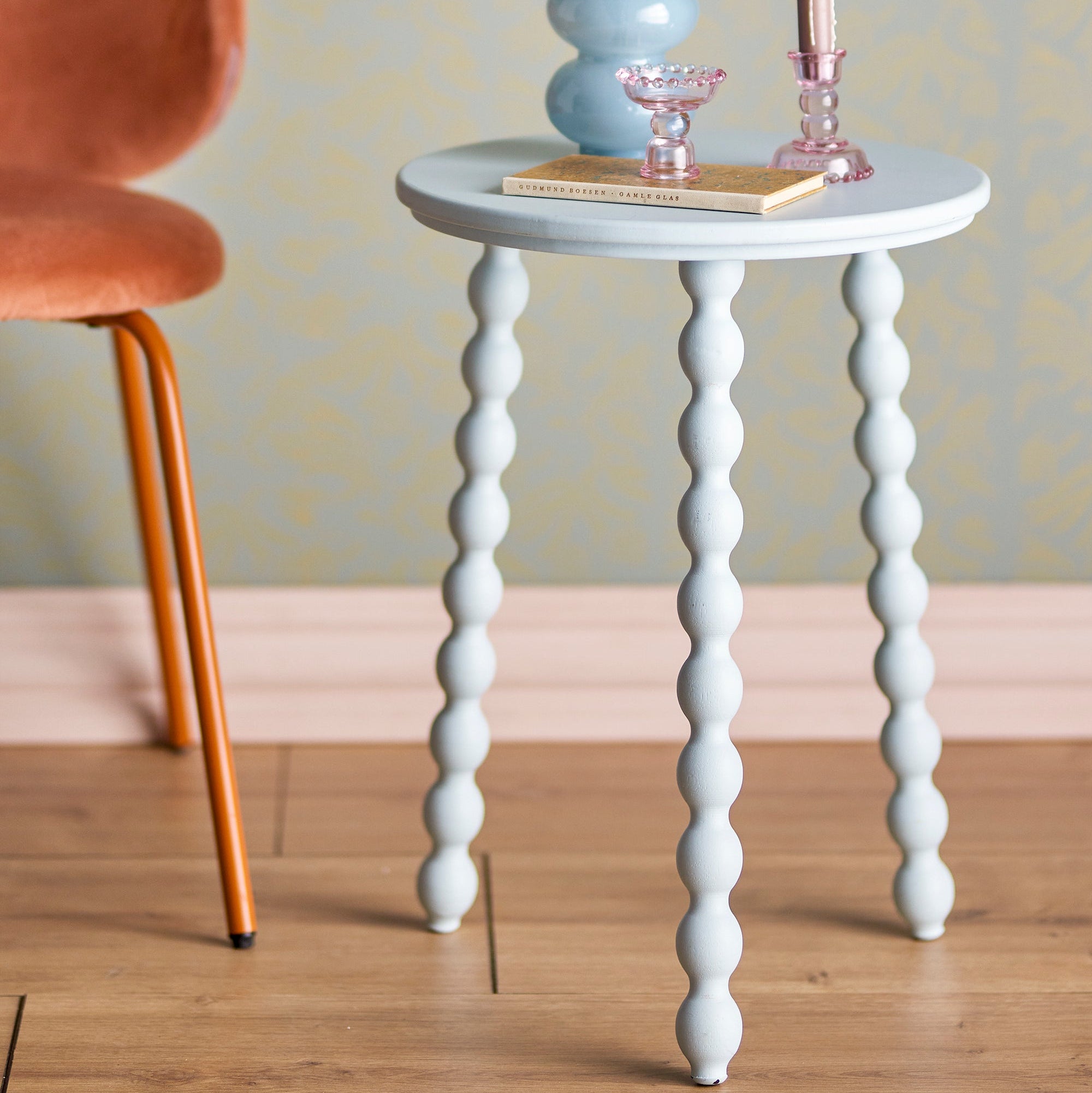 Small round pale blue table with spiral legs in a room setting with a chair and decorative items.