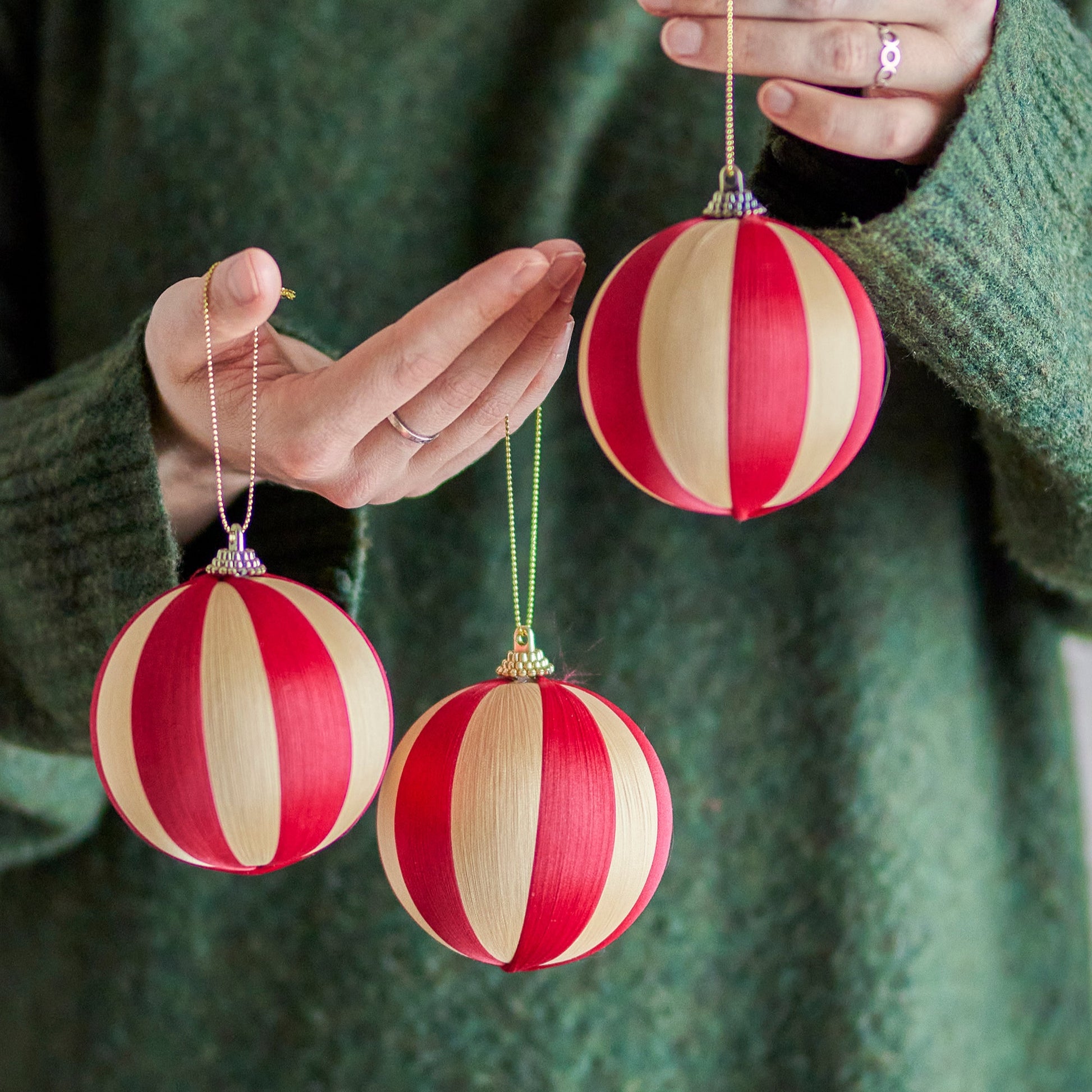 Red and beige striped Christmas ornaments held by a person wearing a green sweater.